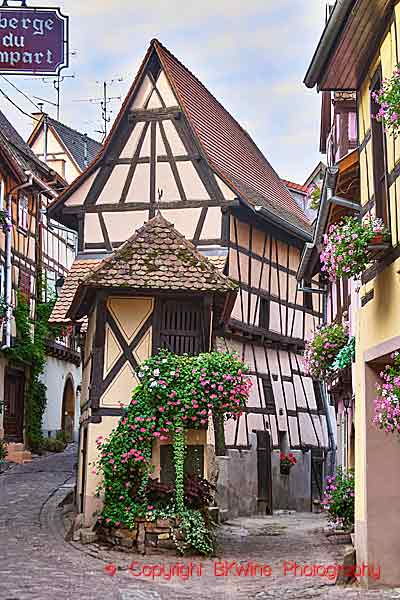 En smal gränd med ett smalt korsvirkeshus med blommor i byn Eguisheim i Alsace